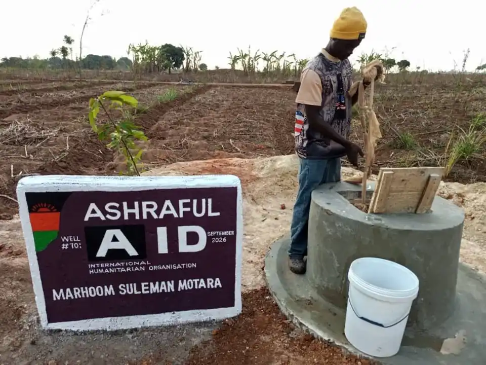 A man drawing water at a completed Ashraful Aid well with its dedication plaque