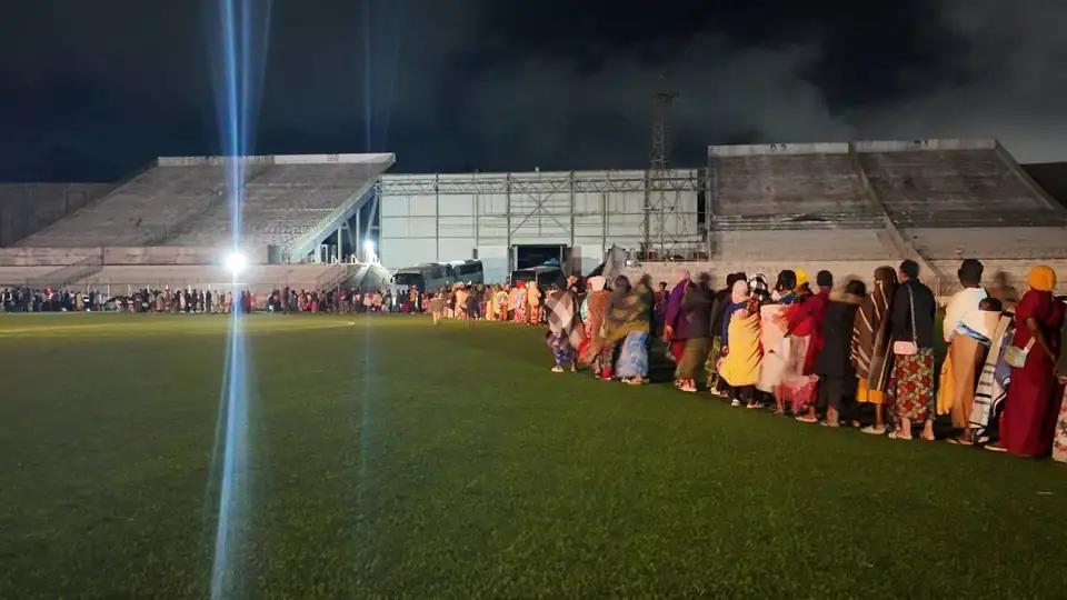 Families queueing in an orderly line at a floodlit stadium for winter support